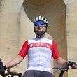 Load image into Gallery viewer, Cyclist with bike and helmet holding wearwell water bottle and wearing cycling jersey in red and white