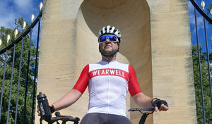 Cyclist with bike and helmet holding wearwell water bottle and wearing cycling jersey in red and white